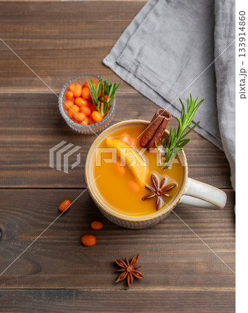 Sea buckthorn herbal tea in a cup on a wooden background with spices, berries and napkin. Sea buckthorn herbal tea in a cup on a wooden background with spices, berries and napkin. 133914860
