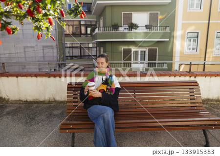 young woman facing camera on bench holding coffee and snack 133915383