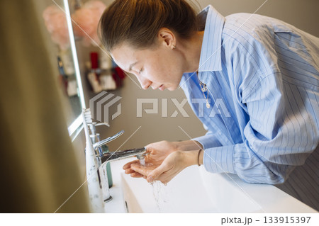 Caucasian woman gently cleansing her face in soft warm light 133915397