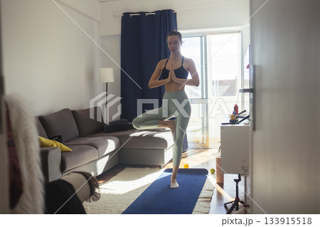 Serene woman maintains tree pose in cozy apartment setting 133915518