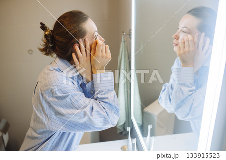 Mirror reflection of woman gently applying cosmetic cream 133915523