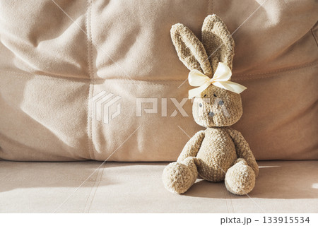 Plush Crocheted Bunny with Yellow Ribbon Sitting on Beige Couch Plush Crocheted Bunny with Yellow Ribbon Sitting on Beige Couch 133915534
