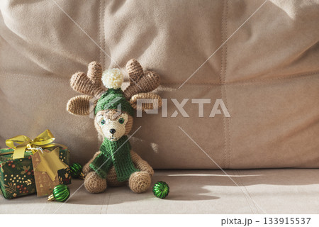 Crocheted Reindeer with Christmas Gift Box and Ornaments on Cozy Holiday Background 133915537