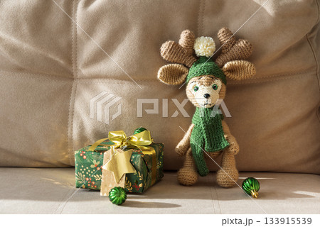 Crocheted Reindeer with Christmas Gift Box and Ornaments on Cozy Holiday Background 133915539