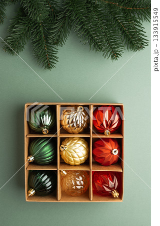 Box of Christmas Ornaments in Festive Colors with Fir Tree Branch on Green Background 133915549