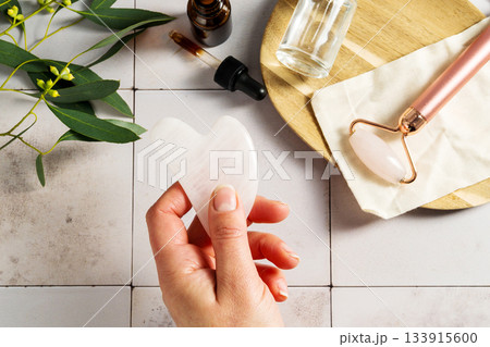 Rose quartz gua sha tool in female hand, face massage tool, beauty abstract photo Rose quartz gua sha tool in female hand, face massage tool, beauty abstract photo 133915600