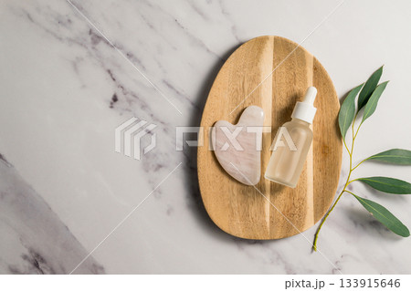 Rose quartz gua sha tool and oil bottle on wooden tray, face massage tool, beauty abstract photo. Copy space Rose quartz gua sha tool and oil bottle on wooden tray, face massage tool, beauty abstract photo. Copy space 133915646