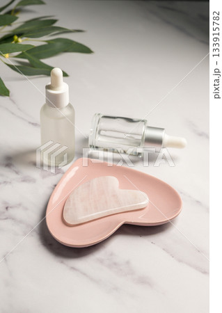 Rose quartz gua sha tool and oil bottles, face massage tool, beauty abstract photo 133915782