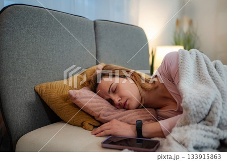 Woman sleeping in bed wearing a smartwatch with phone nearby 133915863
