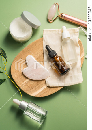 Rose quartz gua sha tool and face massage roller on green background, beauty abstract photo. Top view Rose quartz gua sha tool and face massage roller on green background, beauty abstract photo. Top view 133915874