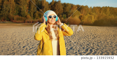 Happy inspired woman enjoying listening to music in headphones outdoors on autumn coast by the sea 133915932