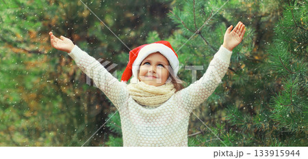 Happy smiling little girl child in santa red hat, snow in forest on Christmas tree background 133915944