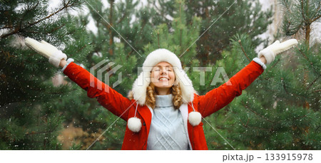 Winter day, happy smiling young woman enjoys snow, warm weather against Christmas tree 133915978