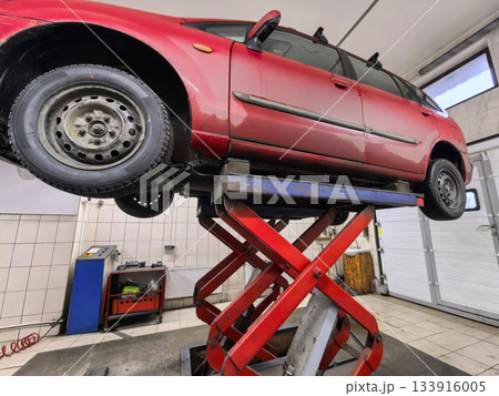 Red sedan elevated on a lift for maintenance in an auto repair shop 133916005