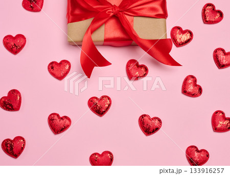 Gift box wrapped in craft paper and tied with a red satin bow on a pink background 133916257