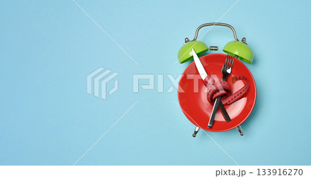 Diet concept image, red plate with crossed cutlery wrapped with red measuring tape stands on green alarm clock face 133916270