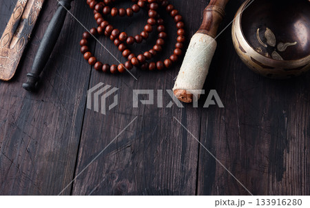 On a wooden background above are traditional meditation items: a Tibetan singing bowl, wooden mala beads On a wooden background above are traditional meditation items: a Tibetan singing bowl, wooden mala beads 133916280
