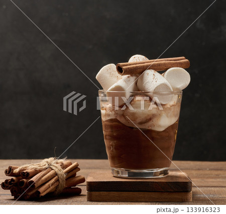 A glass of hot chocolate or cocoa with lots of cinnamon-dusted marshmallows on a wooden background. A glass of hot chocolate or cocoa with lots of cinnamon-dusted marshmallows on a wooden background. 133916323
