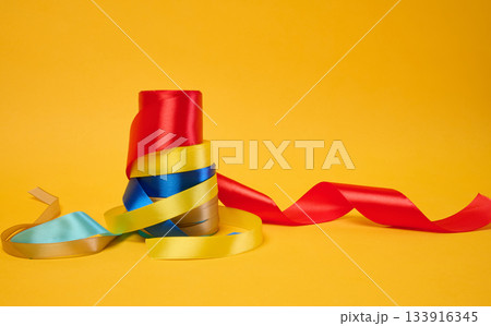 Rolled bright satin ribbons on a yellow background, festive decor 133916345