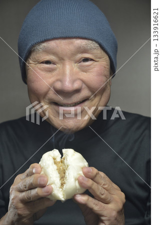 湯気の立ち昇る肉まんを笑顔で食べる老人 133916621