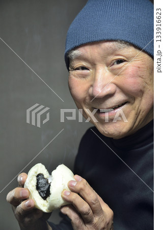 湯気の立ち昇るあんまんを笑顔で食べる老人 133916623