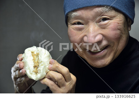 湯気の立ち昇る肉まんを笑顔で食べる老人 133916625