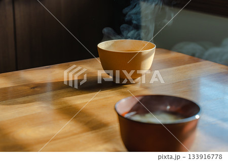 朝の光の中で湯気が立ち上る味噌汁と木のテーブルのある朝食風景 133916778