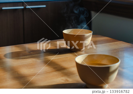 朝の光の中で湯気が立ち上る味噌汁と木のテーブルのある朝食風景 朝の光の中で湯気が立ち上る味噌汁と木のテーブルのある朝食風景 133916782