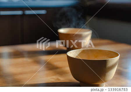 朝の光の中で湯気が立ち上る味噌汁と木のテーブルのある朝食風景 133916783