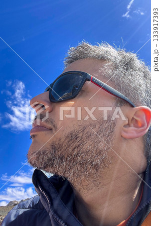A man with a beard and glasses is wearing sunglasses and looking at the camera 133917393