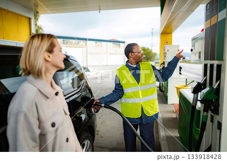 Service worker assisting woman refueling car at gas station 133918428