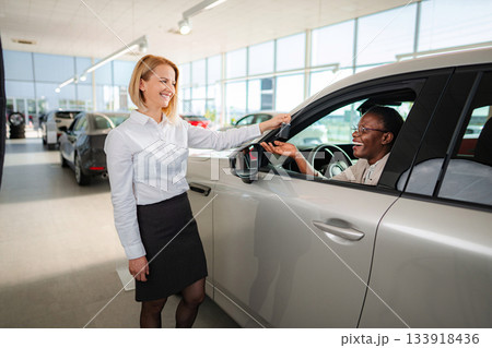 Saleswoman handing over car keys to happy customer 133918436