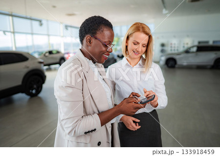 Two women using smartphone in car dealership during sales process 133918459