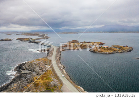 Scenic Atlantic ocean road winds through rugged coastal landscape connecting small islands in calm dark blue waters. Remote and wild beauty of Norway 133919318