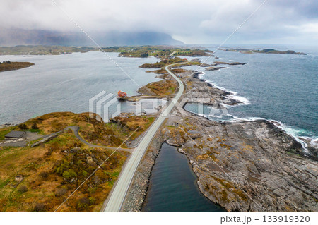 Atlantic ocean road snakes across small islands and skerries at dusk. Reflective water surface under cloudy sky highlights serene beauty of Norway 133919320