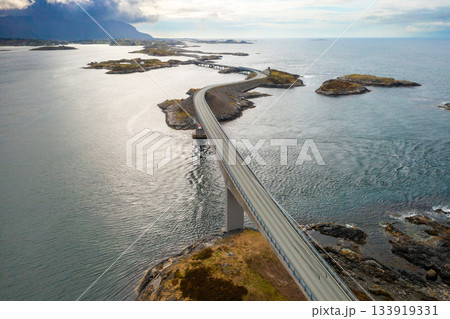 Atlantic ocean road demonstrates impressive span stretching across rocky islets in sea. Highway elegantly curves along path under muted cloudy sky 133919331