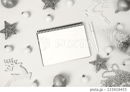 Demonstrating the colors of 2026 - Cloud Dancer. Christmas composition of stars and toys on Christmas tree, with open blank notebook and pen for writing goals and plans for the New Year. 133919455
