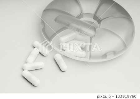 Pills spilling from a clear organizer on a white surface with a neat design 133919760