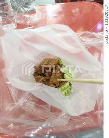 Spicy fried chicken street food plastic bag skewer cucumber red table casual dining night market vibe 133920517