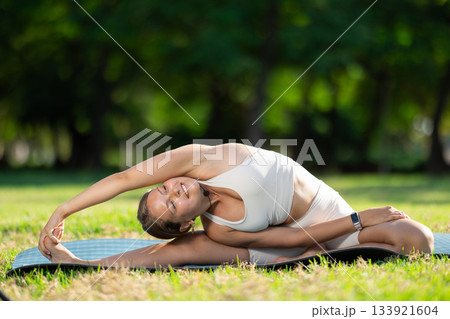 Sporty girl performing yoga asanas on green meadow in summer Sporty girl performing yoga asanas on green meadow in summer 133921604
