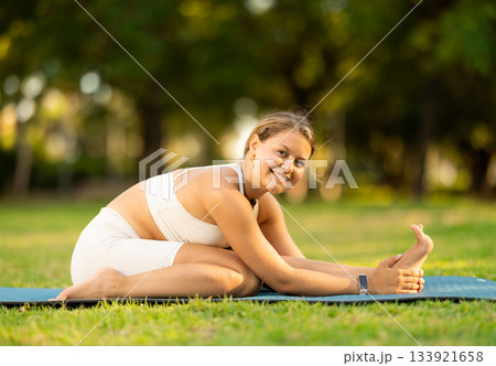 Girl in park on green grass of lawn performs Parivritta Janu Shirshasana Girl in park on green grass of lawn performs Parivritta Janu Shirshasana 133921658