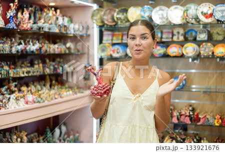 Female buyer holds in hands tests figurine she-dancer flamenco in memorable gifts shop Female buyer holds in hands tests figurine she-dancer flamenco in memorable gifts shop 133921676