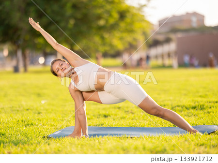 Girl doing Utthita Parsvakonasana yoga asana in summer park 133921712