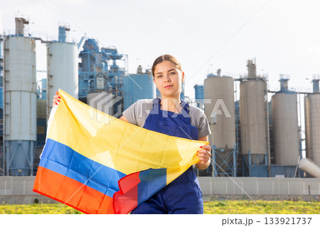 near large plant in Colombian province,calm girl in blue overalls stands and holds flag of Colombia near large plant in Colombian province,calm girl in blue overalls stands and holds flag of Colombia 133921737