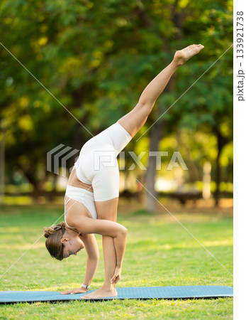 Girl in park on green grass of lawn performs eka padasana Girl in park on green grass of lawn performs eka padasana 133921738