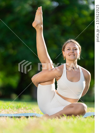 Sporty girl performing yoga asanas on green meadow in summer 133922025