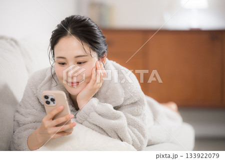 冬のモコモコした部屋着で寝転がるスマホを見る若い女性 133922079