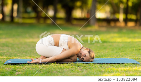 Girl in park on green grass of lawn performs shashankasana Girl in park on green grass of lawn performs shashankasana 133922094