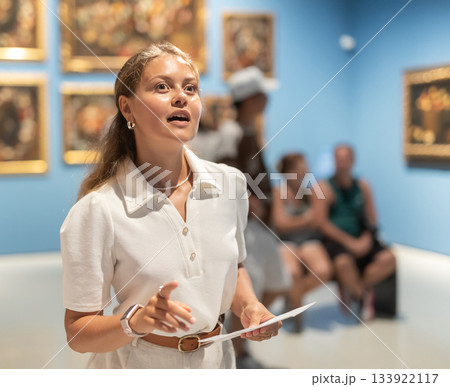 Woman with sheet piece of paper in hands view pictures and icons in museum hall Woman with sheet piece of paper in hands view pictures and icons in museum hall 133922117