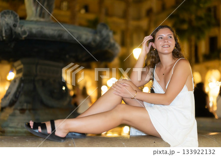 Night Royal square in Barcelona, girl in sundress is sitting on fountain fencing. Night Royal square in Barcelona, girl in sundress is sitting on fountain fencing. 133922132